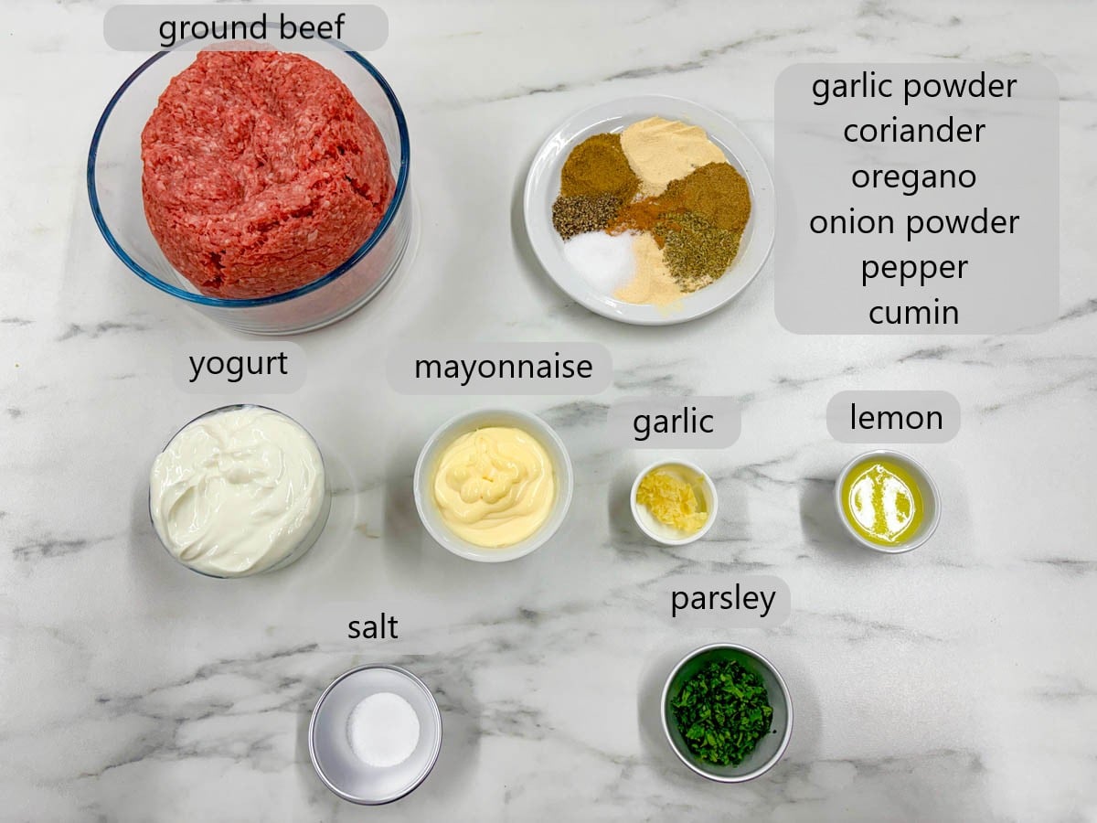 kitchen counter with bowls of ingredients and text overlays reading ground beef, spices, yogurt, mayonnaise, garlic, lemon, salt, and parsley.