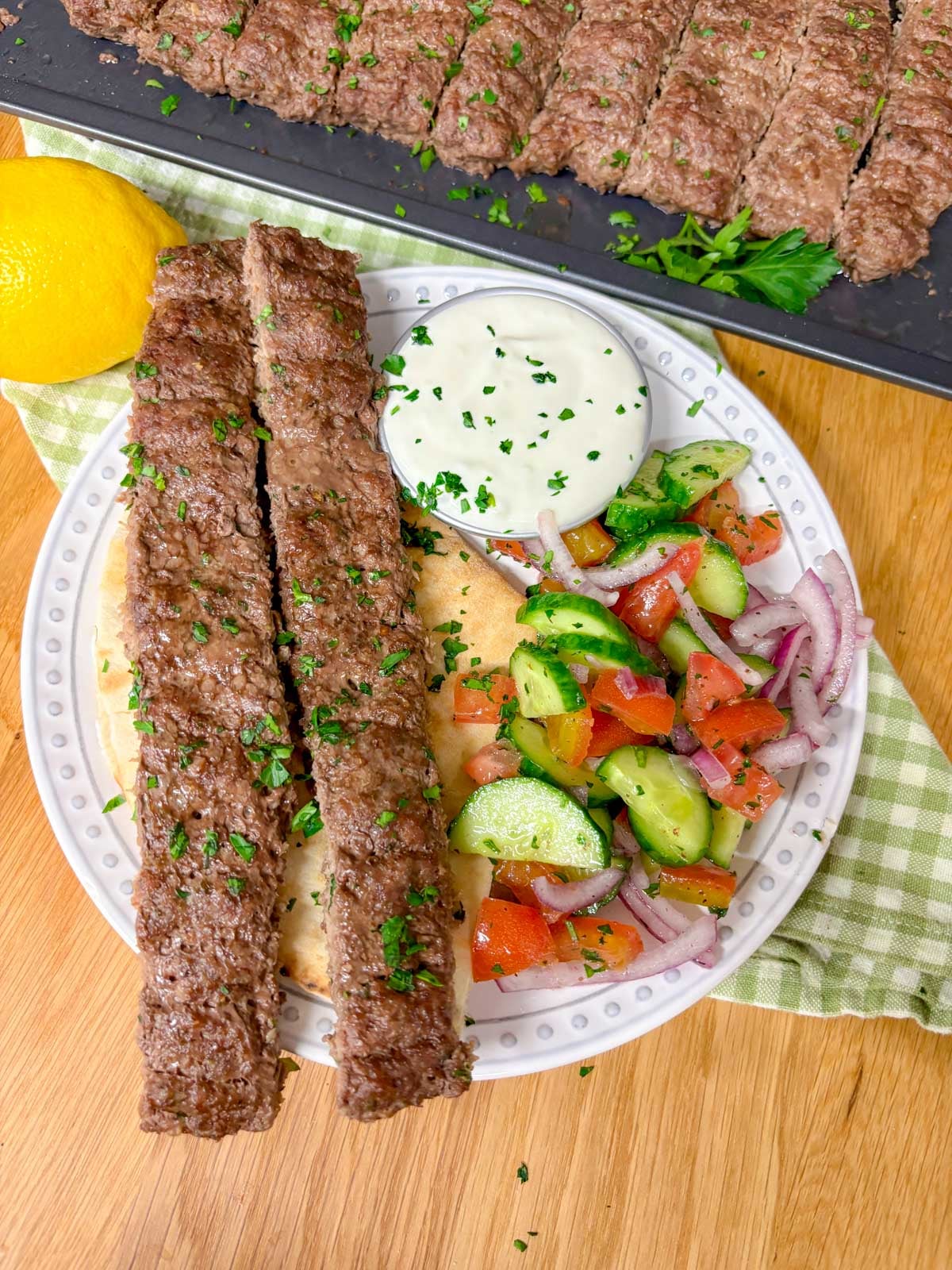 plate with beef kebab, cucumber salad, garlic sauce, and pita bread.