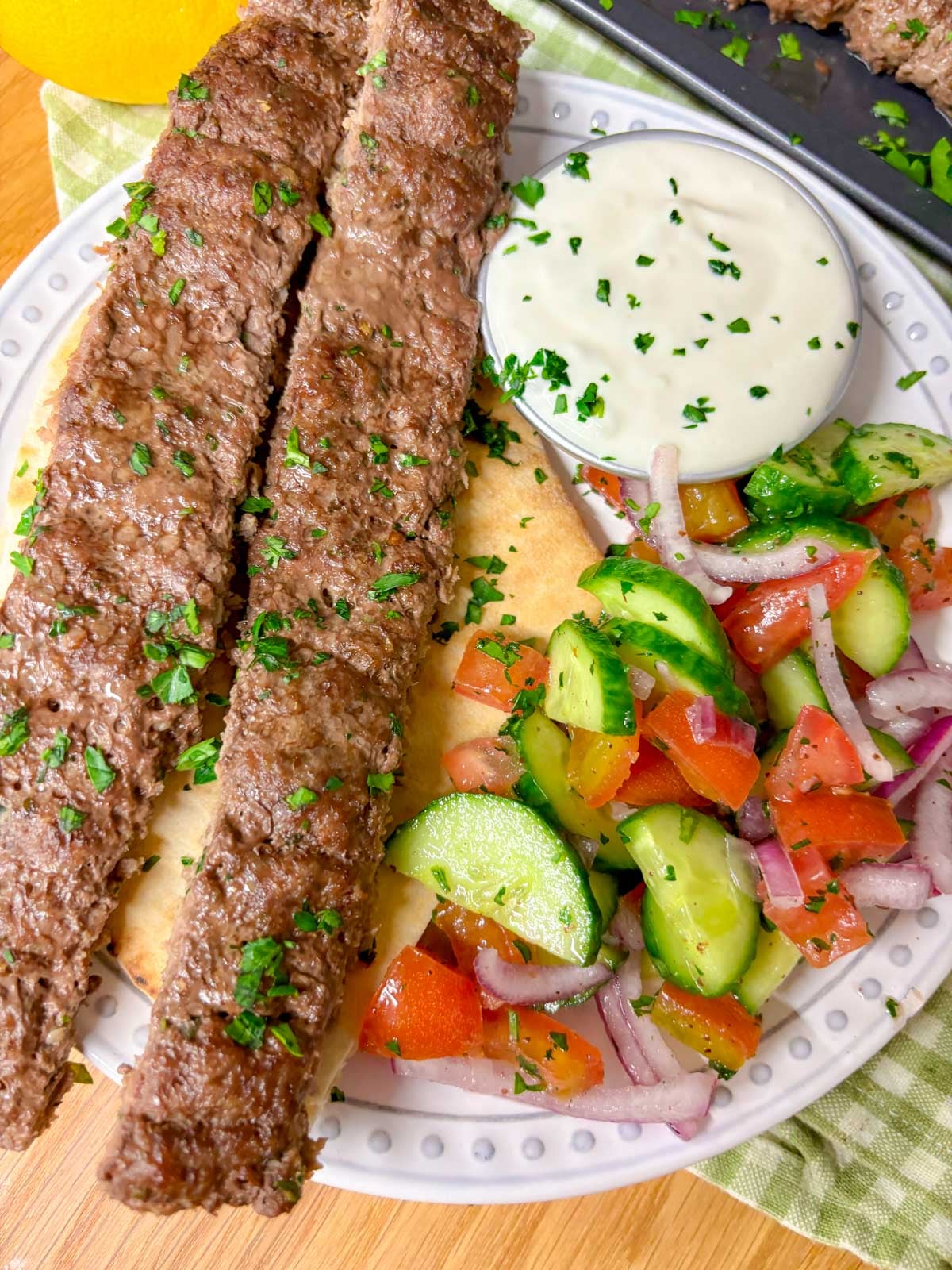 a dinner plate with two beef kebab, pita bread, garlic sauce, and cucumber salad