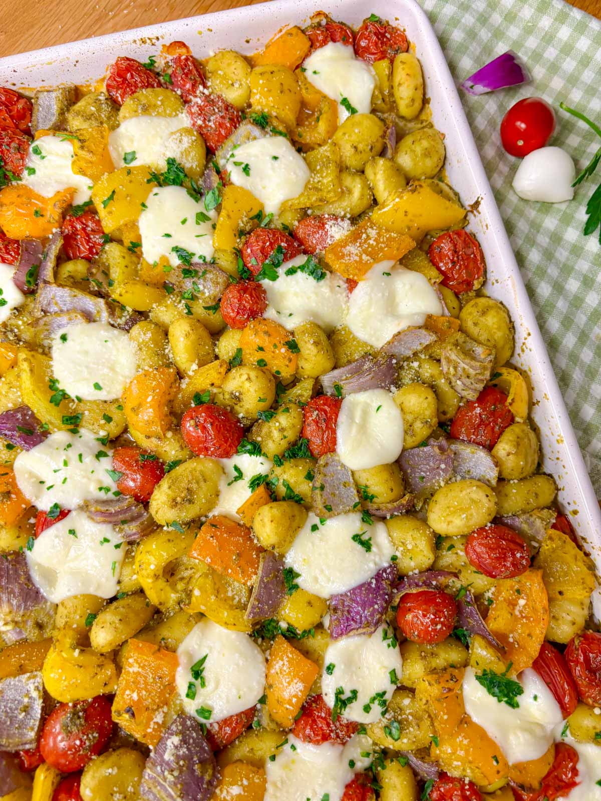 a sheet pan is filled with cheesy pesto gnocchi and garnished with parmesan, basil and parsley