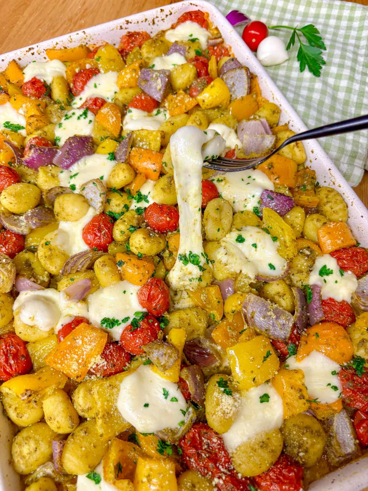 a sheet pan is filled with cheesy pesto gnocchi and garnished with parmesan, basil and parsley.  fork picks up a piece of cheesy gnocchi