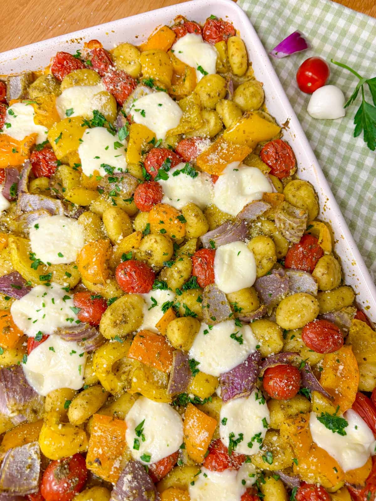 a sheet pan is filled with cheesy pesto gnocchi and garnished with parmesan, basil and parsley