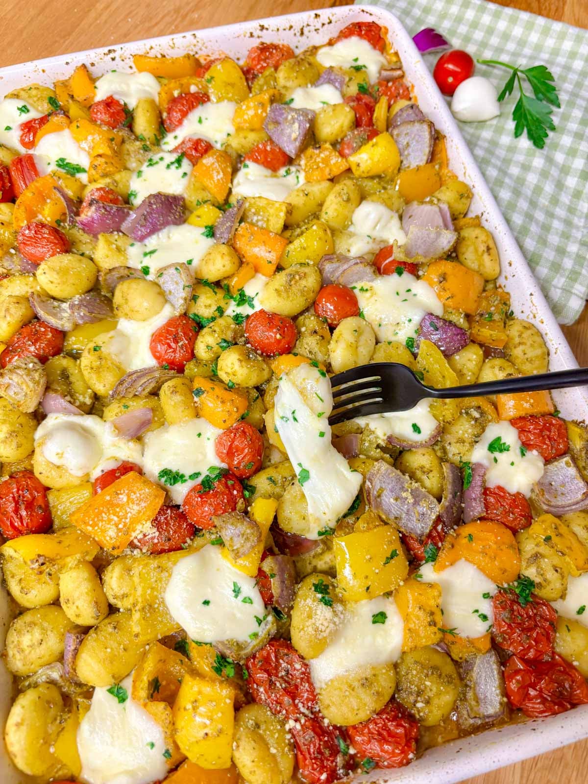 a sheet pan is filled with cheesy pesto gnocchi and garnished with parmesan, basil and parsley. a fork picks up a piece of gnocchi