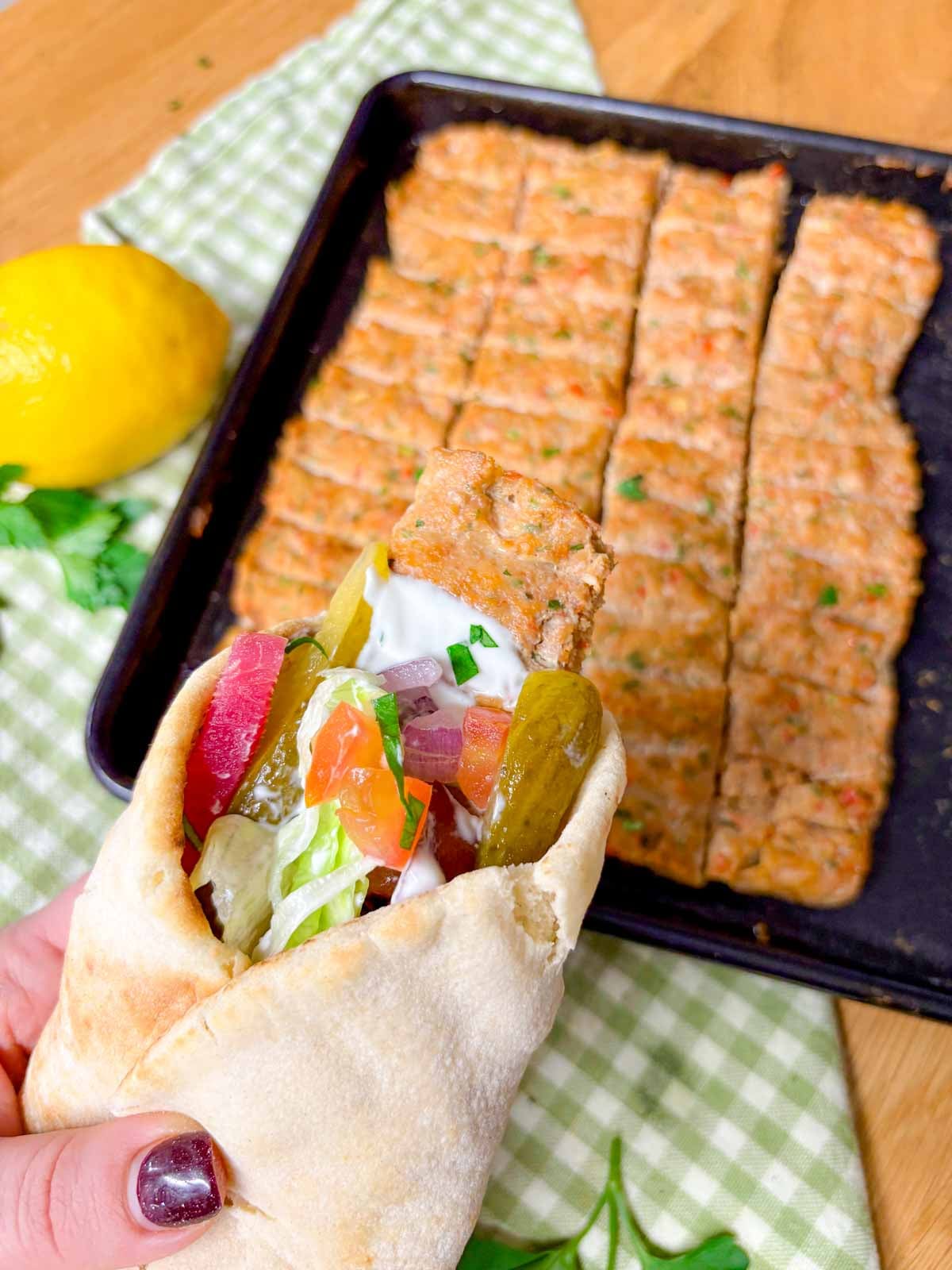 a chicken kebab wrap is held above a baking tray with more kebabs on it