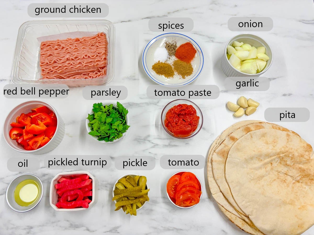 kitchen counter with bowls of ingredients and text overlays reading ground chicken, spices, onion, red bell pepper, parsley, tomato paste, garlic, oil, pickled turnips, pickle, tomato, and pita