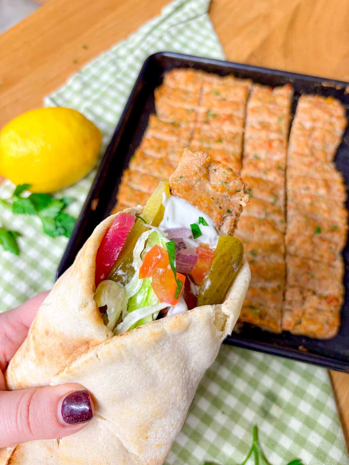 a chicken kebab wrap is held above a sheet pan with more kebabs