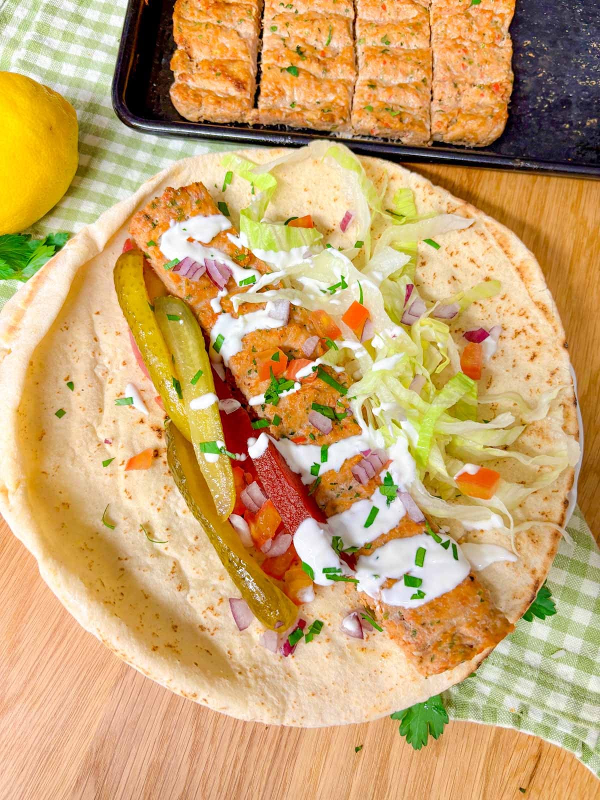 a pit bread is filled with chicken kebab, lettuce, pickles, pickled turnips, tomato, onion, and drizzled with garlic sauce.