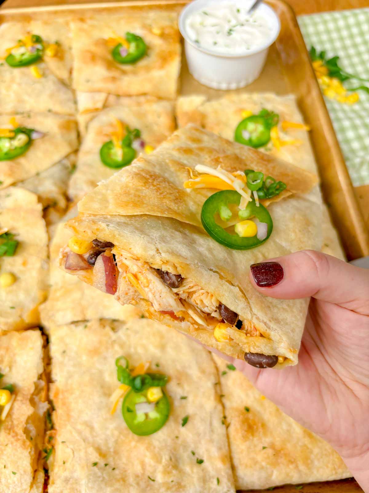 a sheet pan is filled with a loaded chicken quesadilla and cut into 12 pieces. one is held close to camera