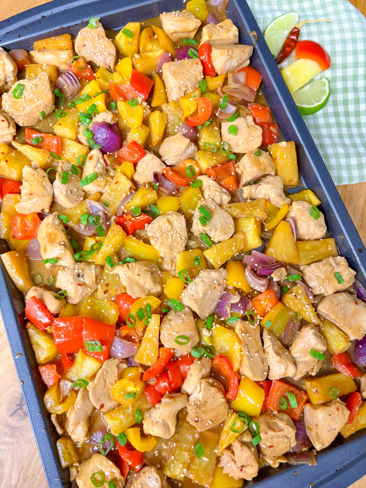 a sheet pan is filled with pineapple chicken stir fry and garnished with green onions and sesame seeds.