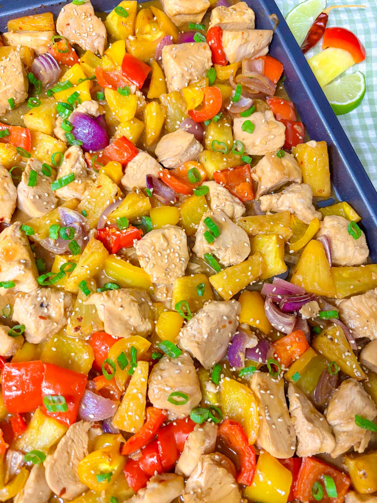 a sheet pan is filled with pineapple chicken stir fry and garnished with green onions and sesame seeds.