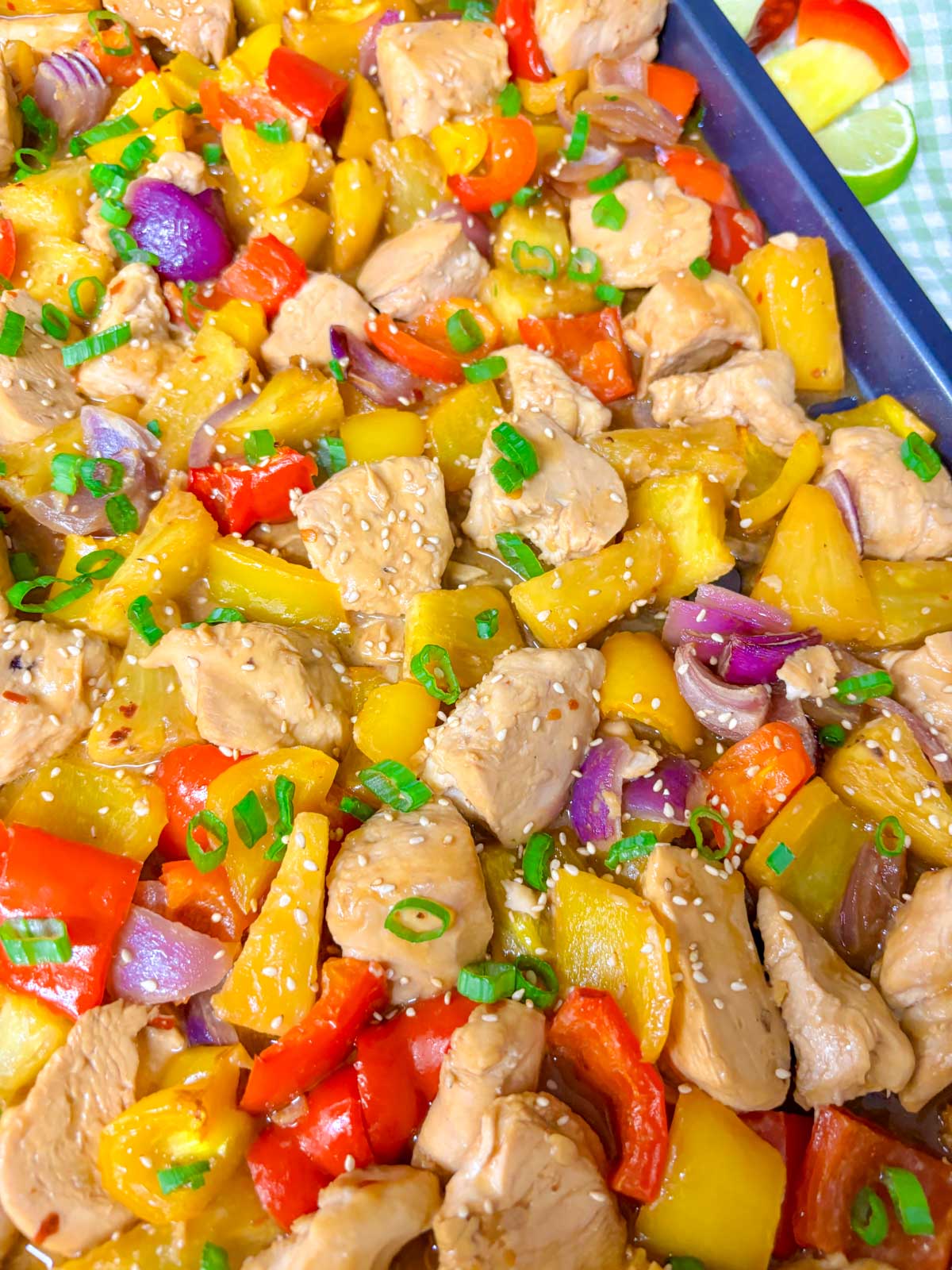 a sheet pan is filled with pineapple chicken stir fry and garnished with green onions and sesame seeds.