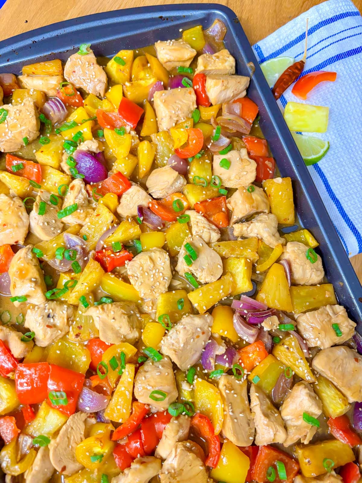 a sheet pan is filled with pineapple chicken stir fry and garnished with green onions and sesame seeds.