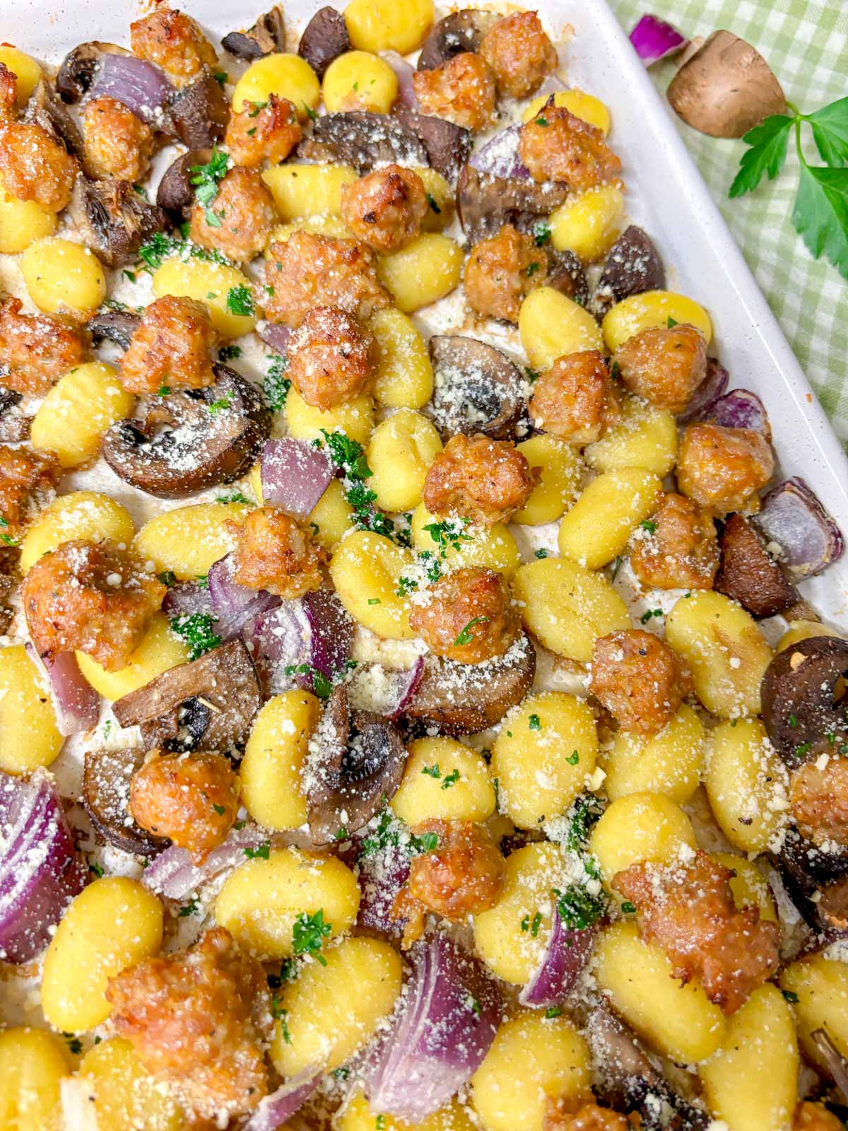 a sheet pan is filled with cooked gnocchi, sausage, mushrooms and red onion. It is garnished with parmesan cheese and parsley.
