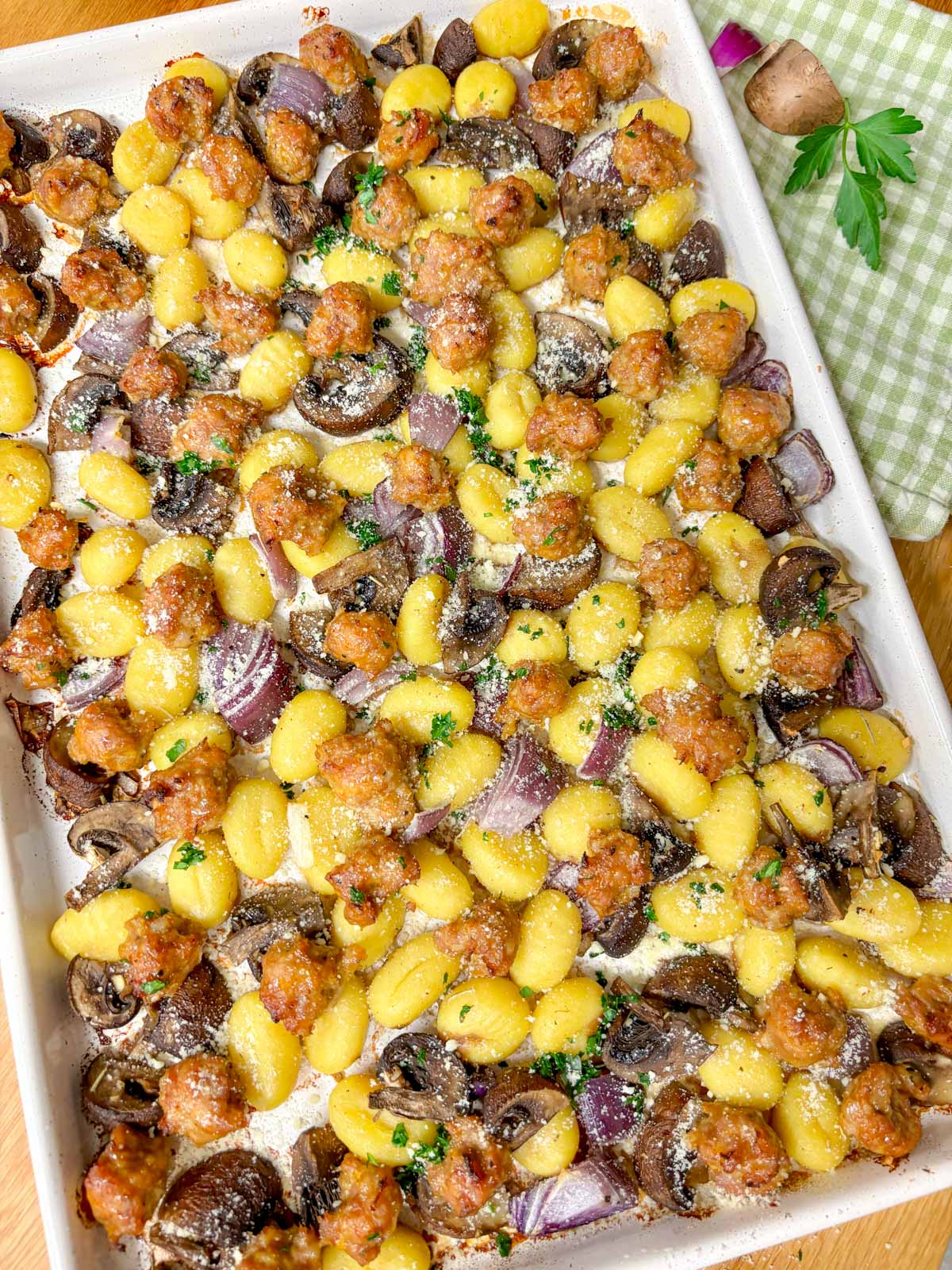 a sheet pan is filled with cooked gnocchi, sausage, mushrooms and red onion. It is garnished with parmesan cheese and parsley.