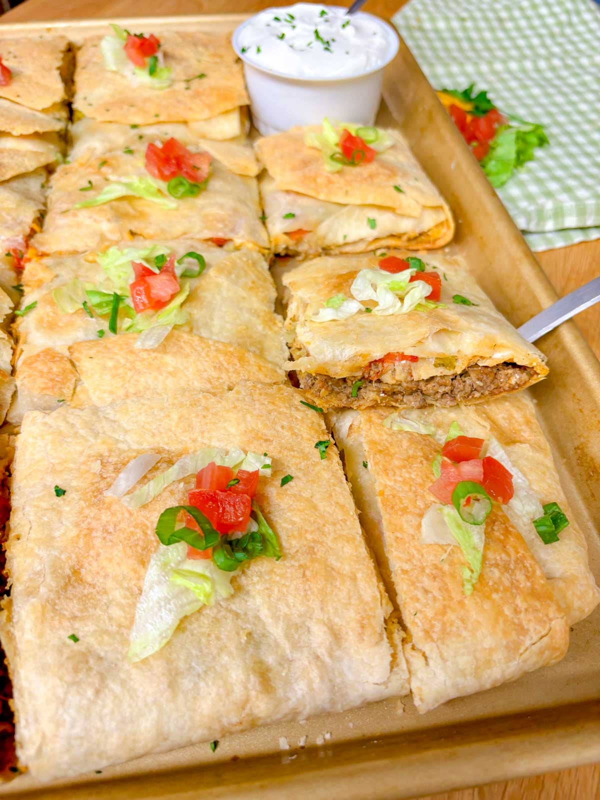 a sheet pan is filled with taco bell crunch wrap supremes with a side bowl of sour cream