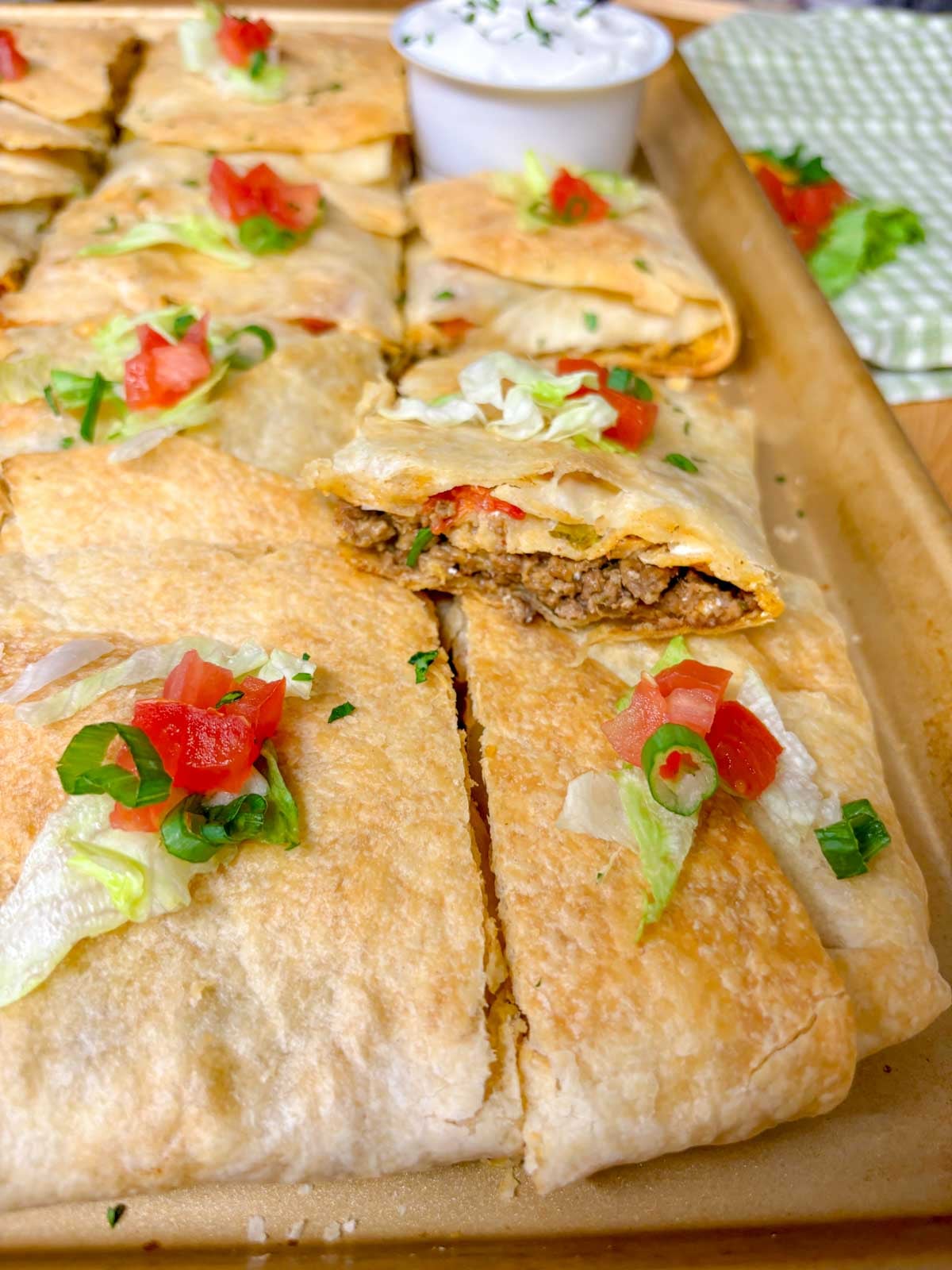 a sheet pan is filled with taco bell crunch wrap supremes with a side bowl of sour cream