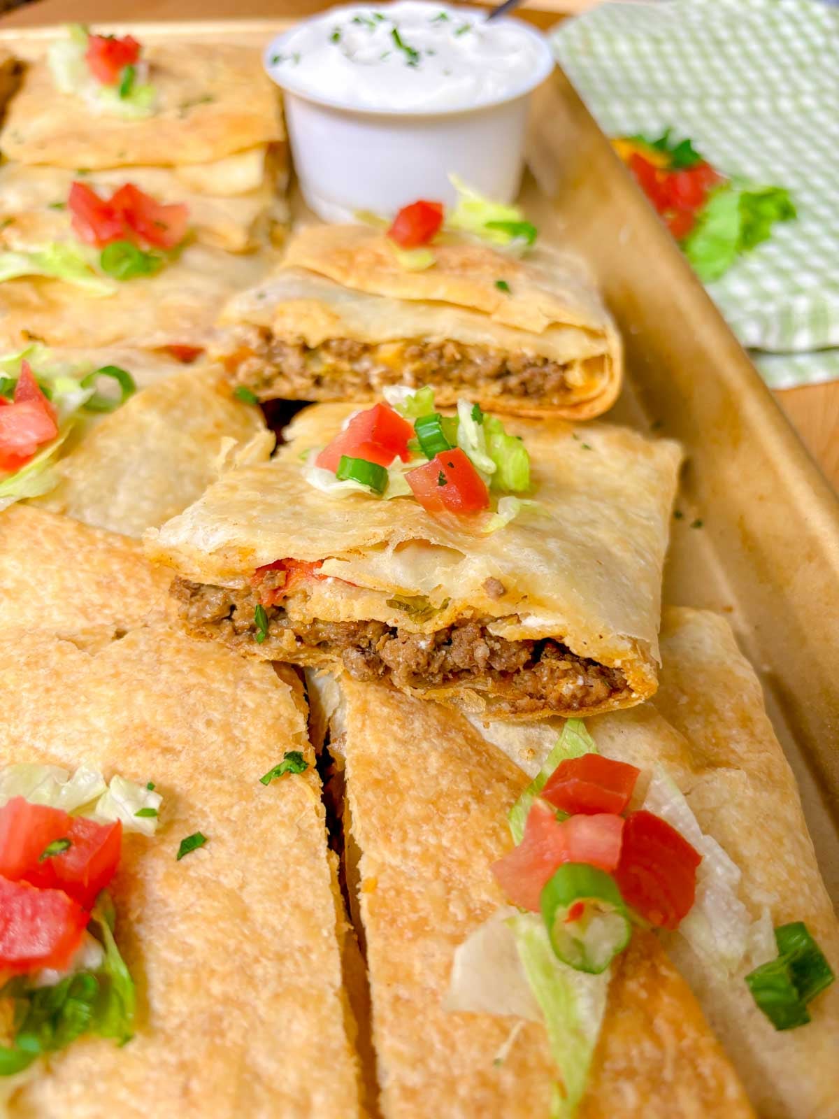 a sheet pan is filled with taco bell crunch wrap supremes with a side bowl of sour cream