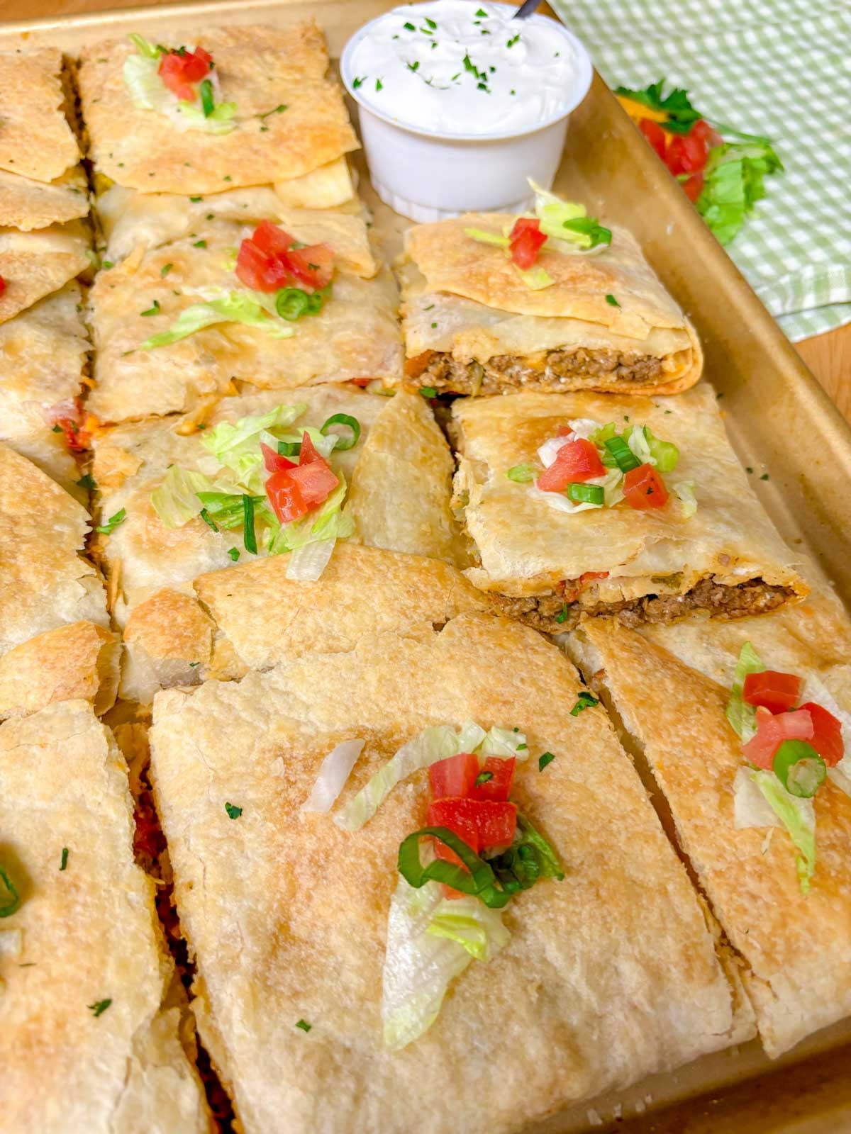 a sheet pan is filled with taco bell crunch wrap supremes with a side bowl of sour cream