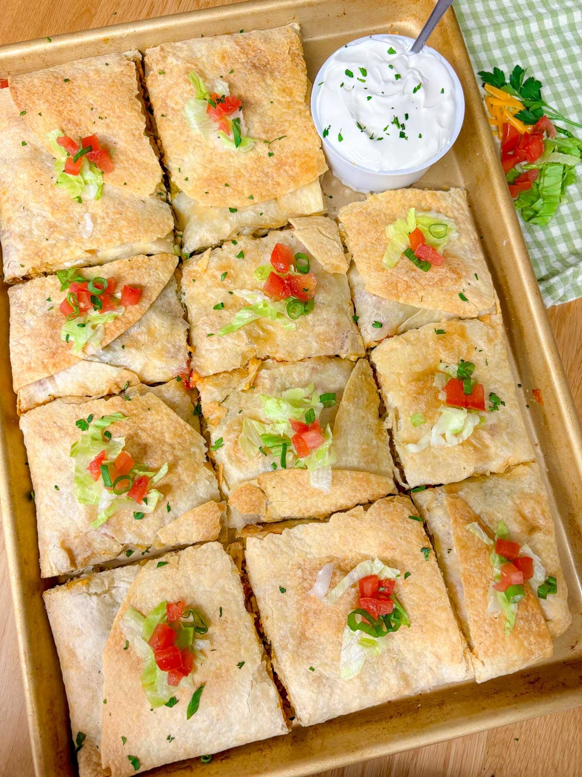 a sheet pan is filled with taco bell crunch wrap supremes with a side bowl of sour cream
