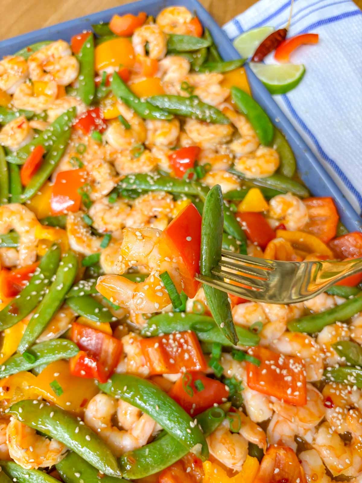 a fork pierces a shrimp, a red bell pepper, and a snow pea. the baking tray is in the background