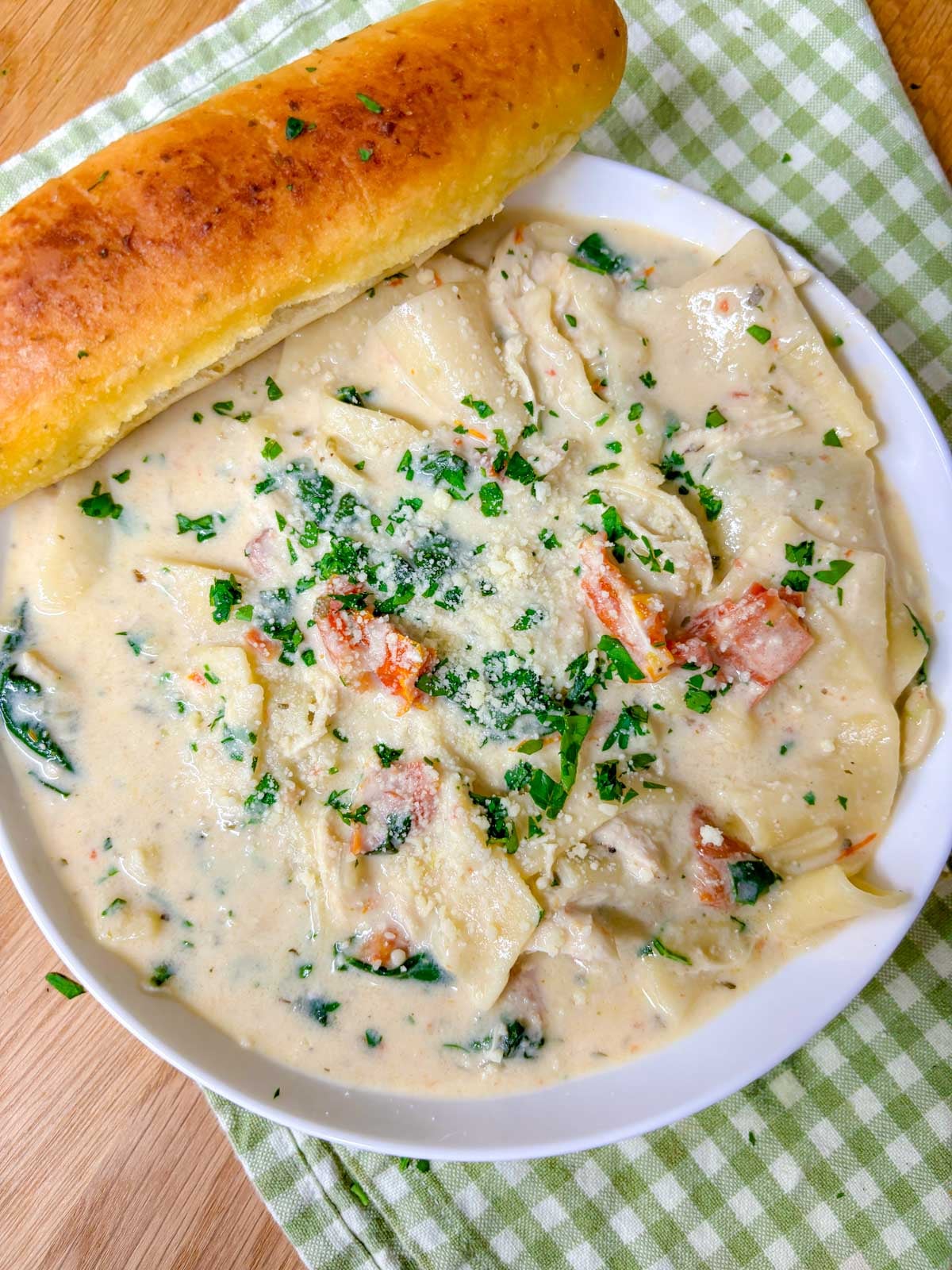 a white bowl is filled with white chicken lasagna soup. a breadstick is on the side