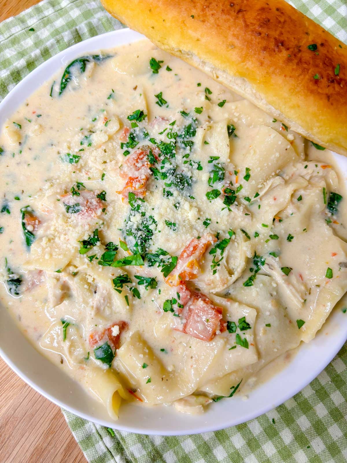 a white bowl is filled with white chicken lasagna soup. a breadstick is on the side