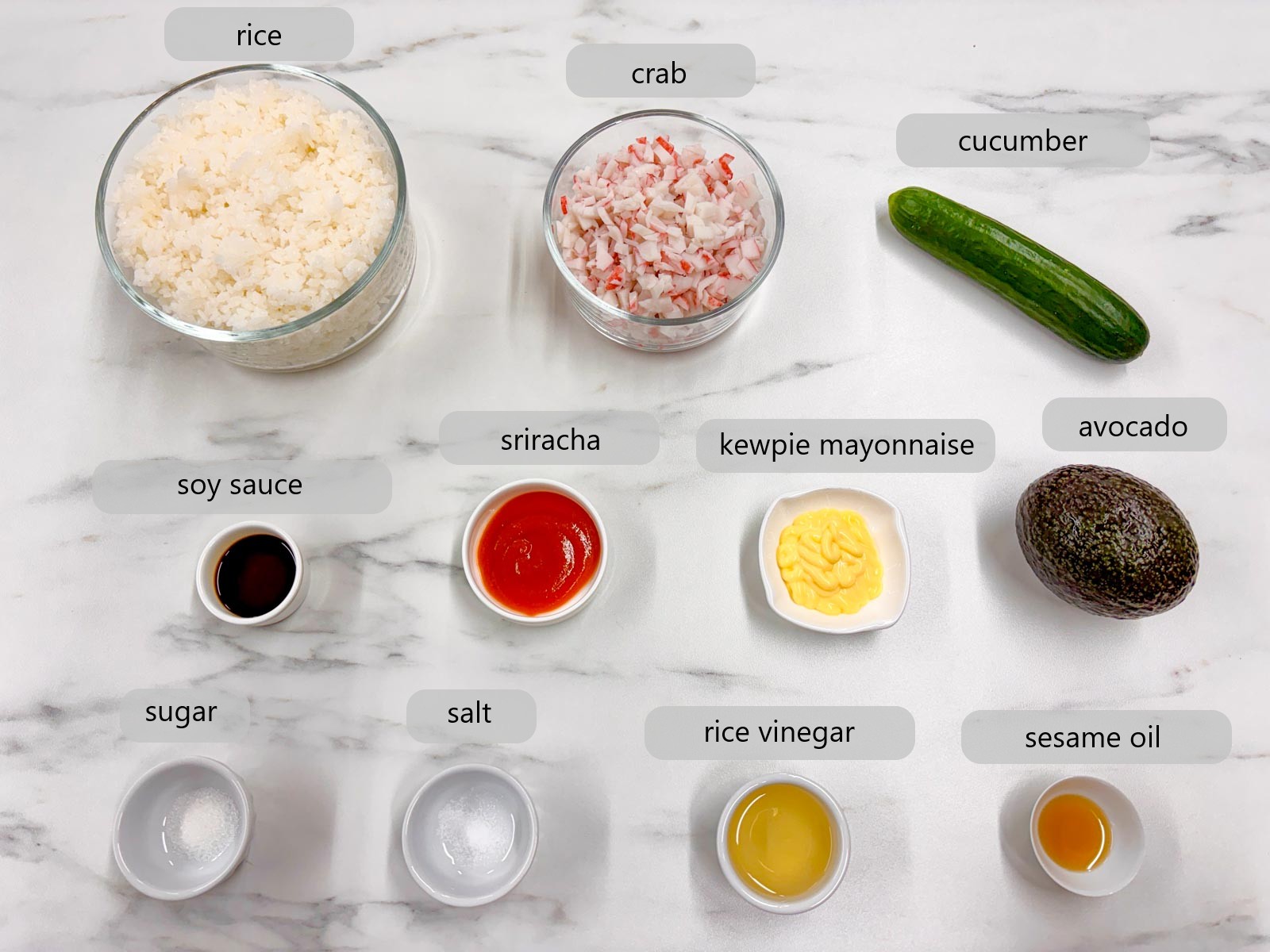 kitchen counter with ingredients and text overlays reading rice, crab, cucumber, soy sauce, sriracha, kewpie mayonnaise, avocado, sugar, salt, rice vinegar, and sesame oil.