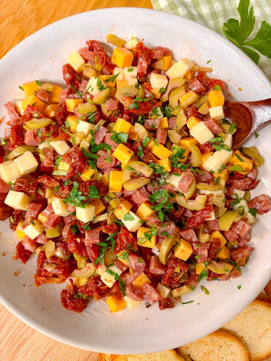 a white bowl filled with charcuterie dip and crostini around the bowl