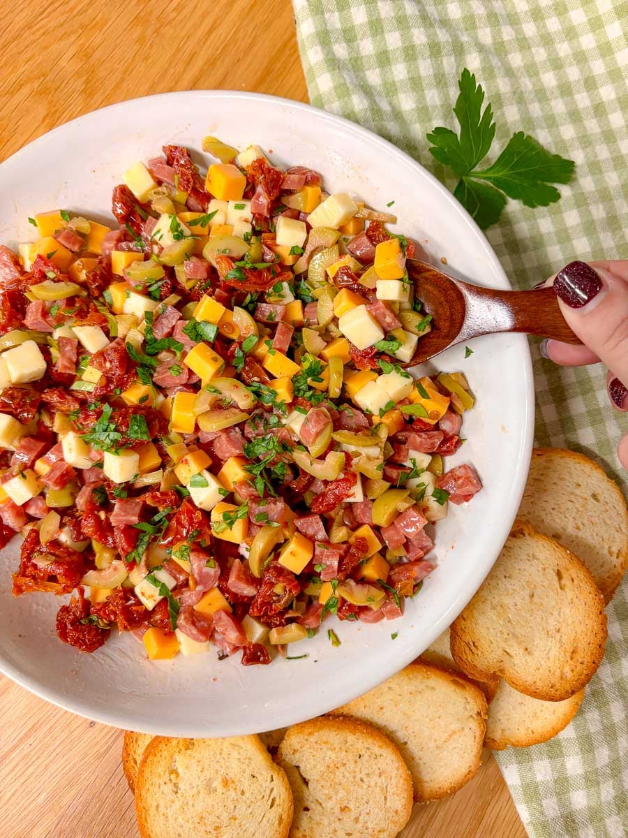a hand uses a wooden spoon to scoop up some of the charcuterie dip