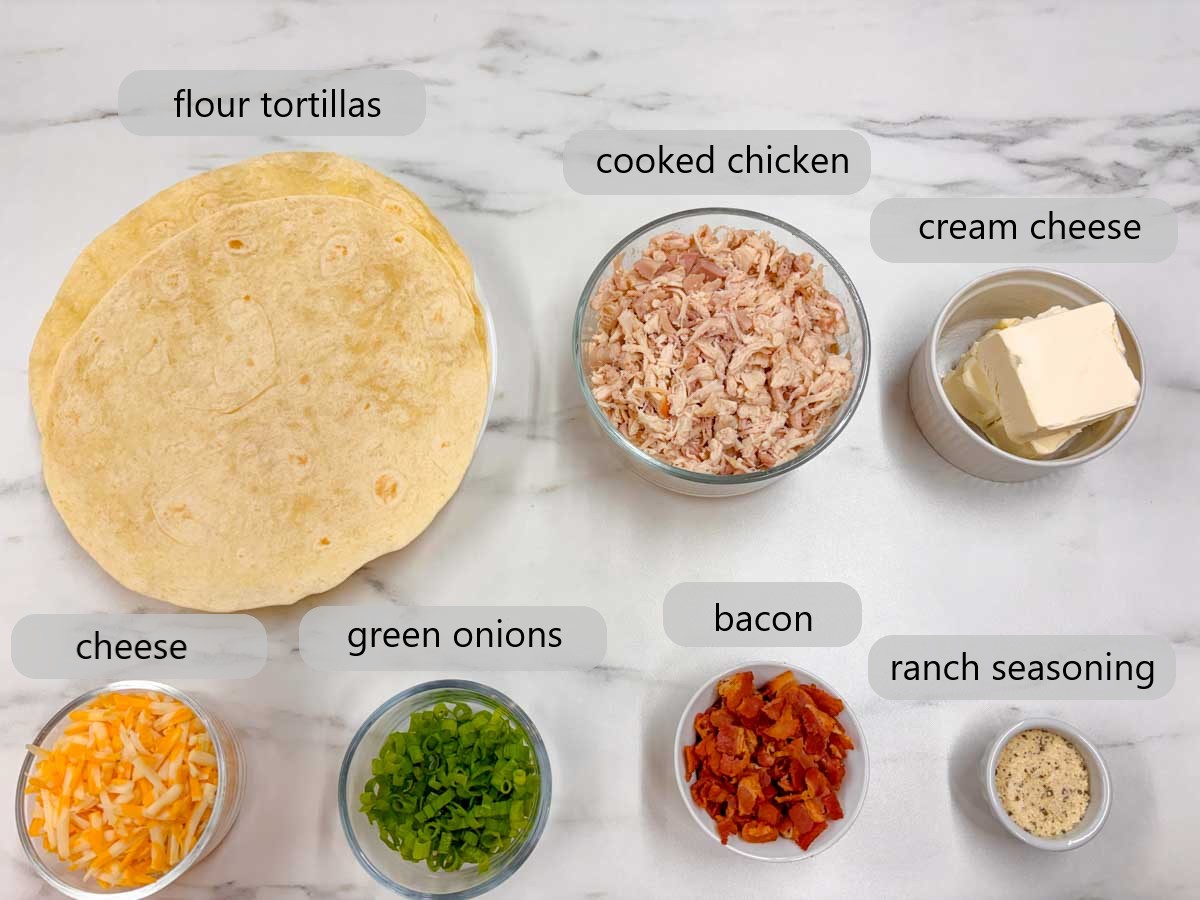 kitchen counter with ingredients and text overlays reading flour tortillas, cooked chicken, cream cheese, cheese, green onions, bacon, and ranch seasoning.