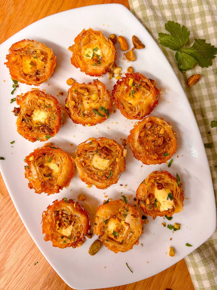 a white platter is filled with crispy baked feta bites and garnished with pistachios