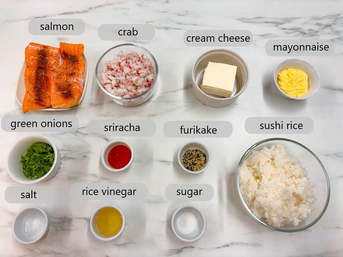kitchen counter with bowls and ingredients and text overlays reading. salmon, crab, cream cheese, mayonnaise, green onions, sriracha, furikake, sushi rice, salt, rice vinegar, and sugar.